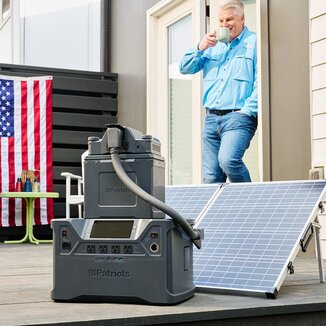 A man standing on his back porch drinking coffee while his Patriot Power Solar Generator charges using his 100-watt solar panel.