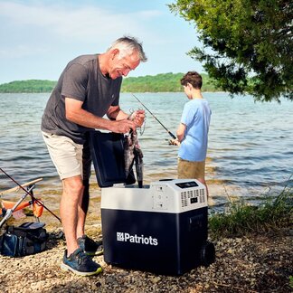 A man fishes by a lake with his grandson on a sunny day using his Solar-Go Fridge to keep fish they catch cold.