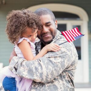 A military man embraces his young daughter who is holding an American flag after returning home from active duty.