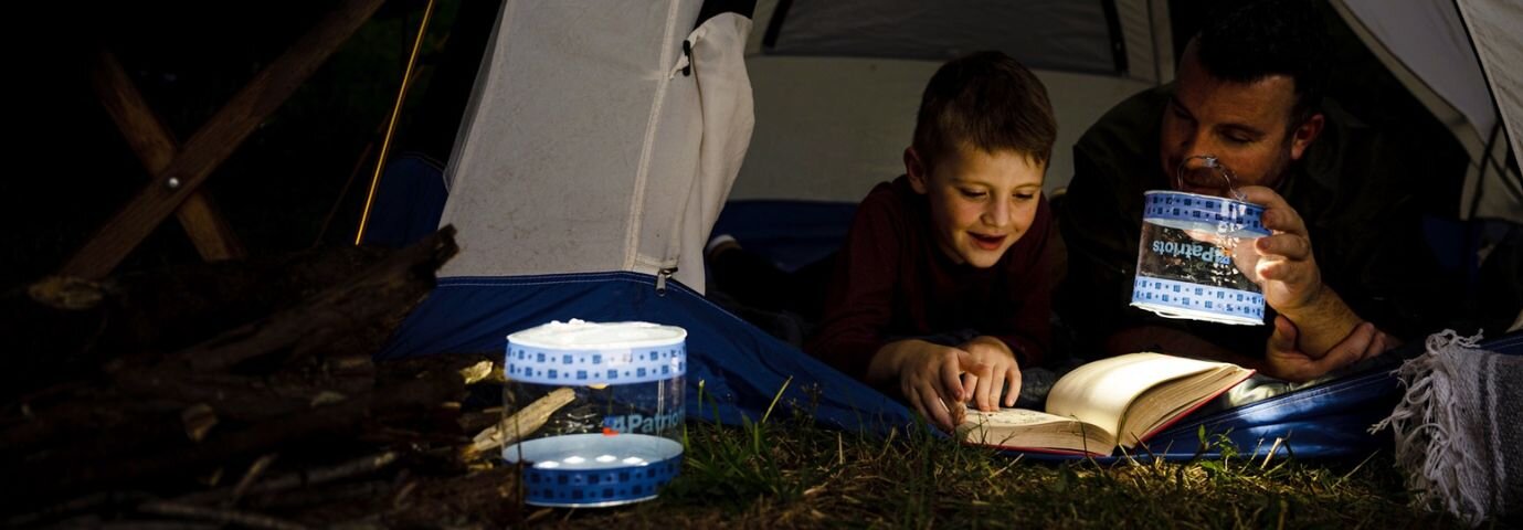 A father and son read at night in their tent using the 4Patriots SoLantern Air as a light.