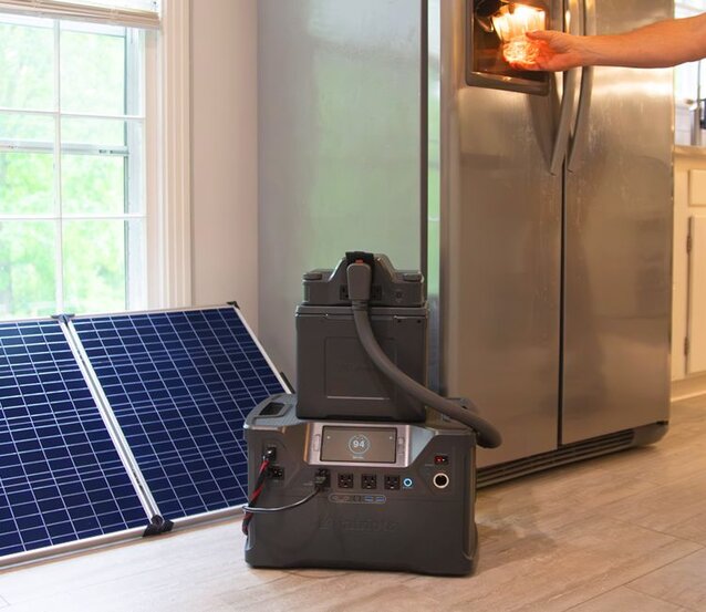 The Patriot Power Generator 2000X in a kitchen powering a man's refrigerator while the solar panel is next to it by the window charging it. 