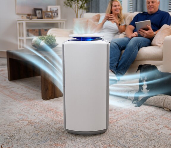 Man and women sitting on a couch in their living room with the Air Advanced Purification System running in the corner. 