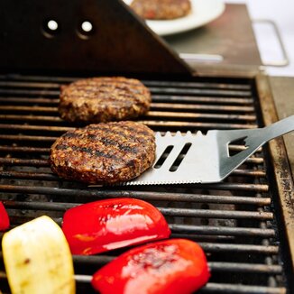 A man grills a black bean burger outside on his patio.
