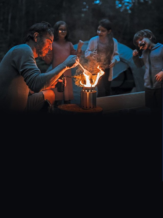 A family of 4 outside at night camping in the woods while they cook dinner on the StarFire Campstove