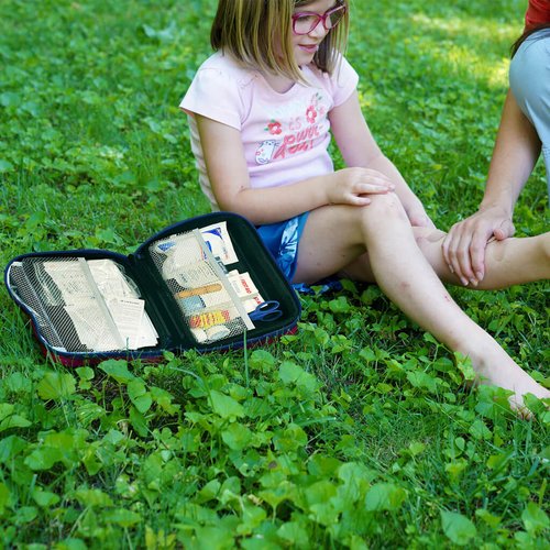 Lifeline Deluxe first aid kit next to a child sitting in the grass getting a bandaid put on her leg.