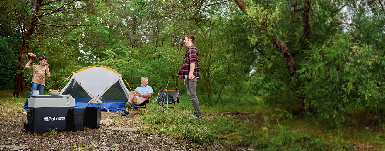 A grandpa, father, and son throwing a football in the woods next to their tent and their Solar Go Fridge as they camp. 