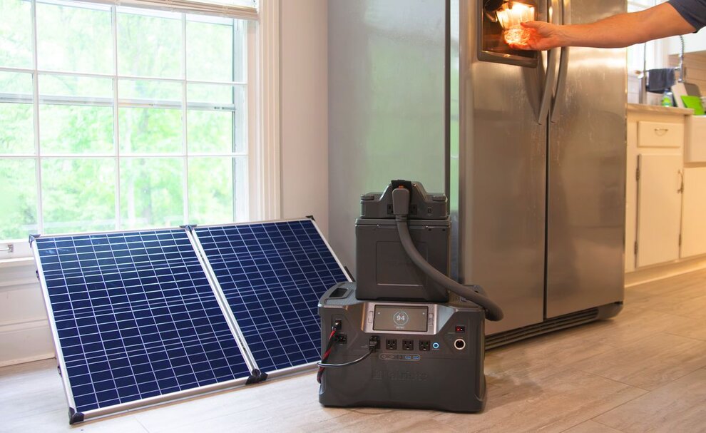 The Patriot Power Generator 2000x in a kitchen powering a man's refrigerator while the solar panel is next to it by the window charging it. 