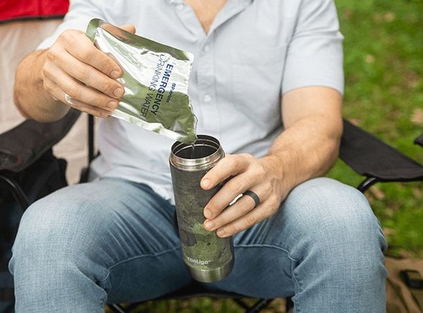 Man sitting outside pouring 4Patriots Emergency Drinking Water pouch into a water container