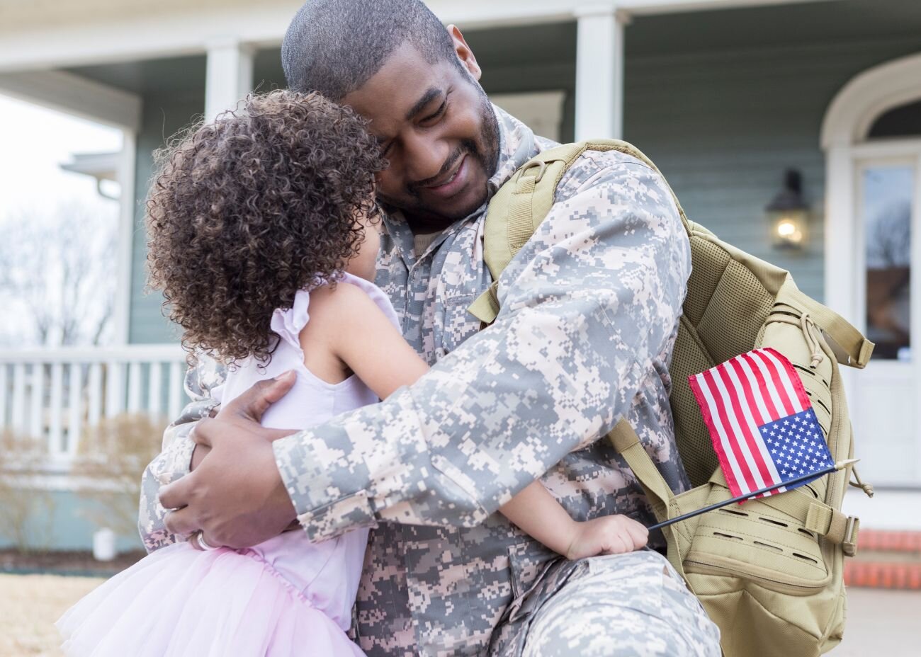 A military dad hugs his young daughter outside their home after returning from deployment.
