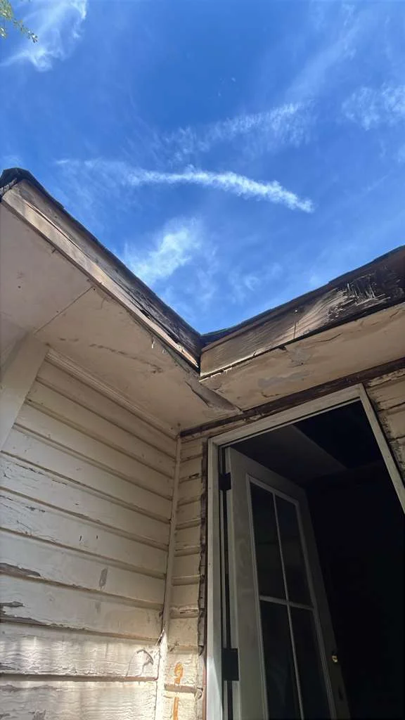 Close-up of rotted fascia and soffit at the entry of a white wood-sided home