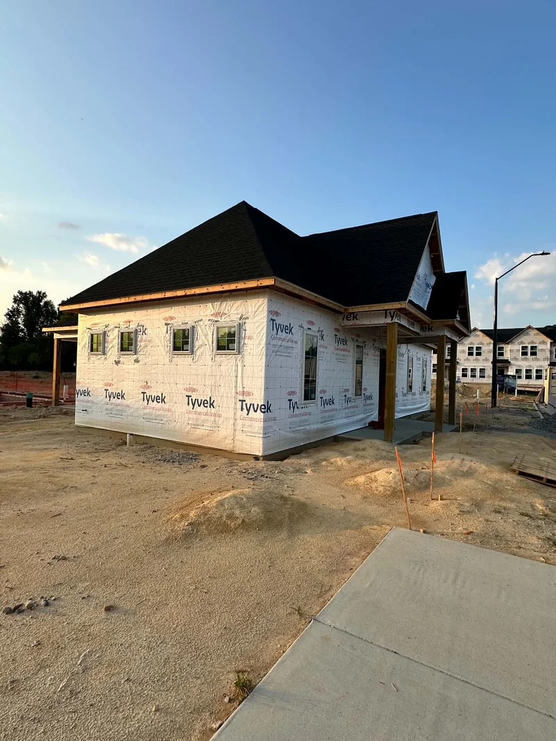 Angled view of new home framing wrapped in Tyvek with covered porch and sidewalk