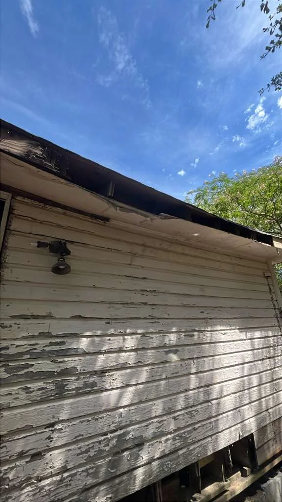 Weathered white wood-sided home with peeling paint and damaged roof trim