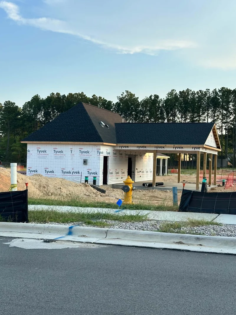New construction home wrapped in Tyvek with dark shingle roof and covered carport
