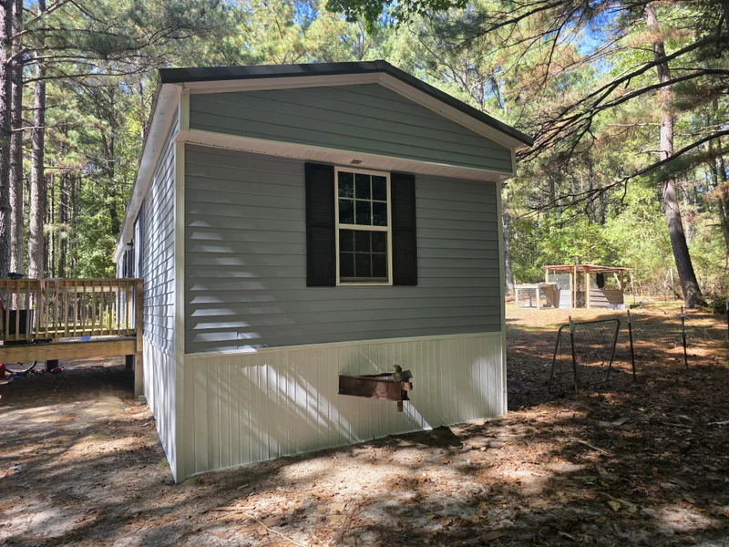 Sage green vinyl-sided manufactured home with black shutters and white skirting