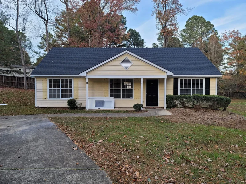 Yellow-sided ranch home with black front door and dark shingle roof