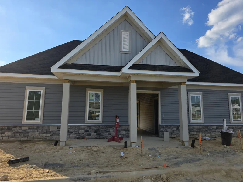 New gray-blue vinyl-sided home with stone skirting and gabled front porch under construction