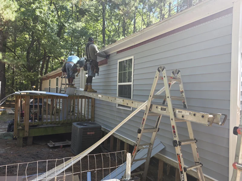 Crew installing light gray vinyl siding on a manufactured home from ladders