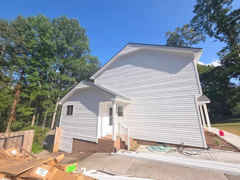Two-story home with white vinyl siding and brick skirting, side view