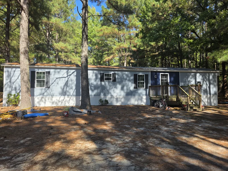 Finished light gray manufactured home with navy accent door, deck, and black shutters