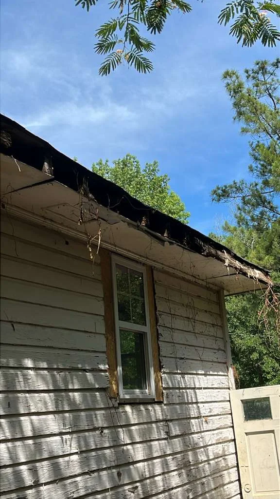 Damaged eave and soffit above a window on a peeling white wood-sided home