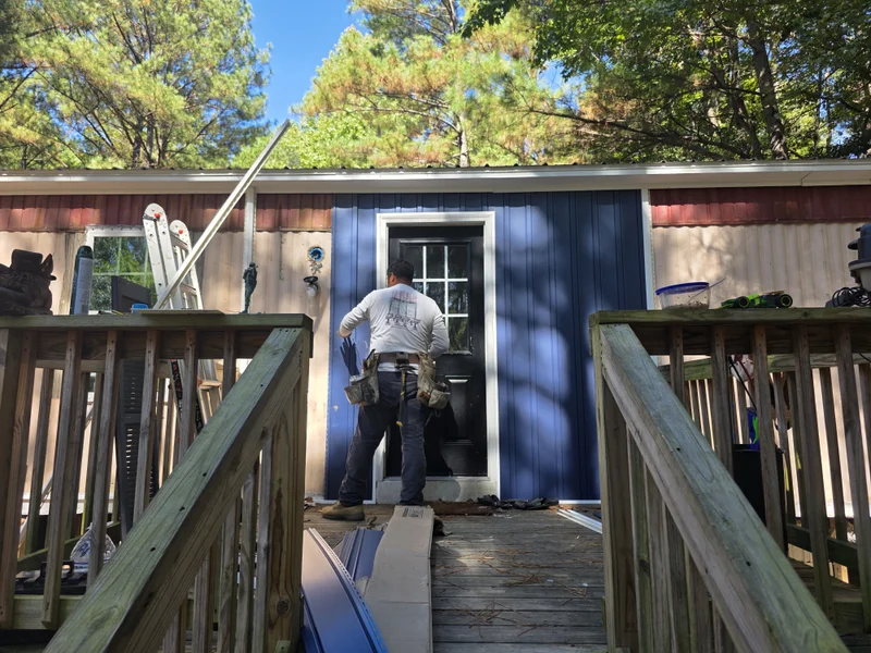 Worker installing a navy vinyl door surround on a manufactured home during re-siding