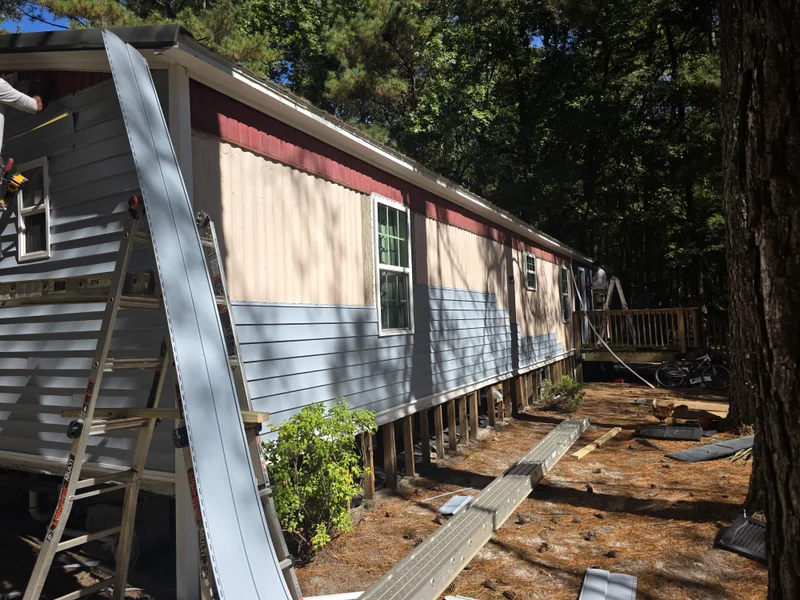 Manufactured home partially re-sided in gray vinyl with tan metal panels still showing