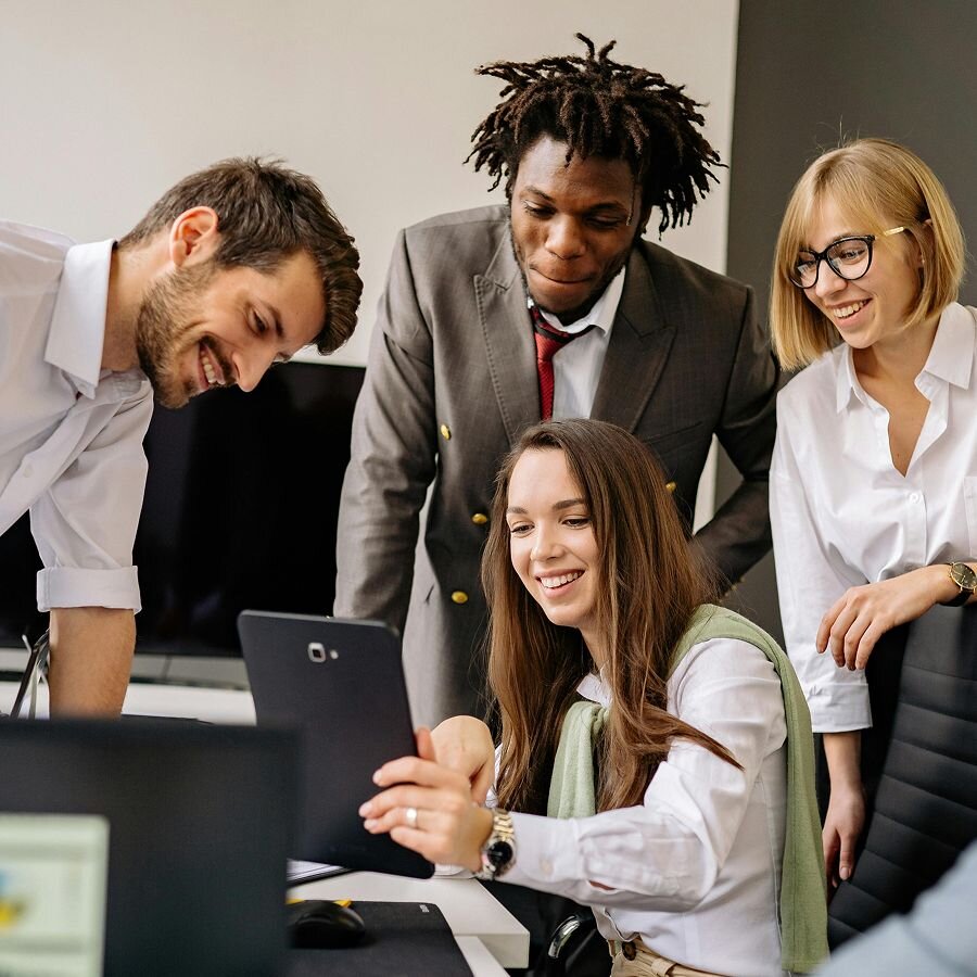 Group of coworkers smiling while gathered around a tablet.