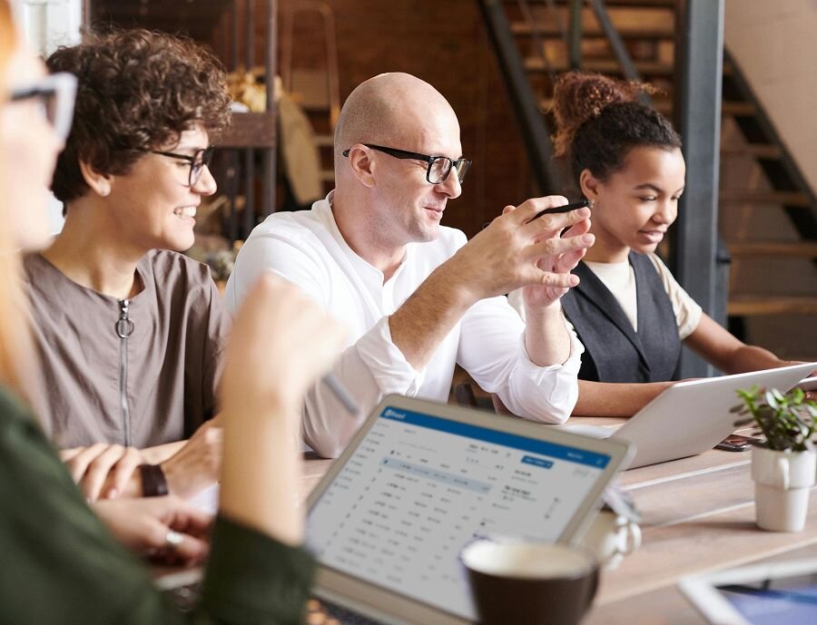 Group of coworkers smiling while seated around a meeting table, some working on laptops.