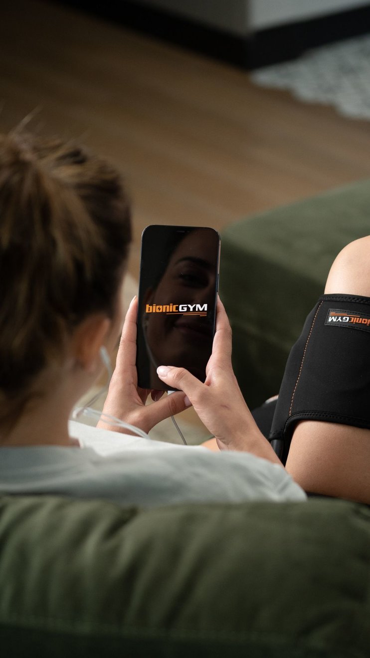 A lady sits on her couch using the BionicGym mobile app to control her BionicGym workout.