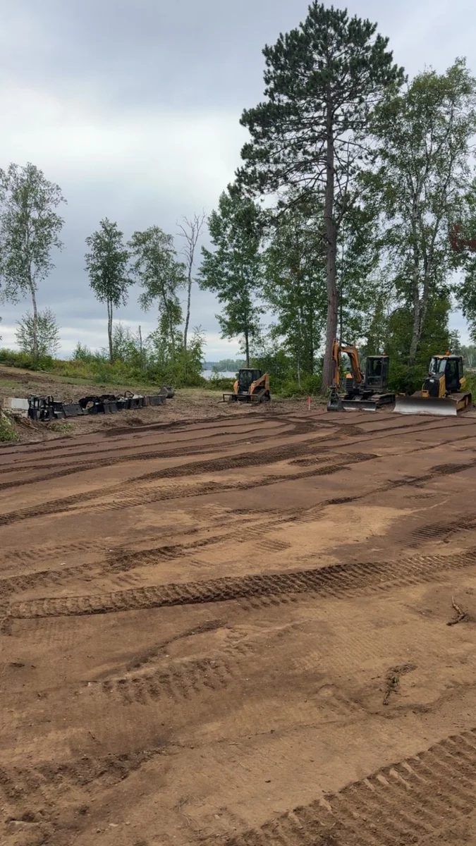 Excavation equipment preparing a dirt site beside mature trees