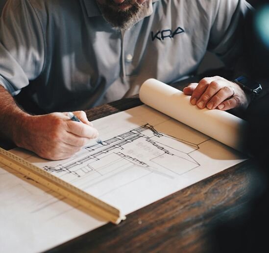 A man sits at a table, focused on working with a blueprint spread out in front of him.