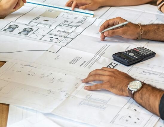 Several individuals focused on reviewing and discussing blueprints, surrounded by drafting tools and materials.