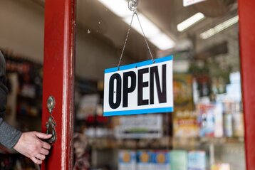 Open sign on a shop door with hand on the knob pushing the door open.