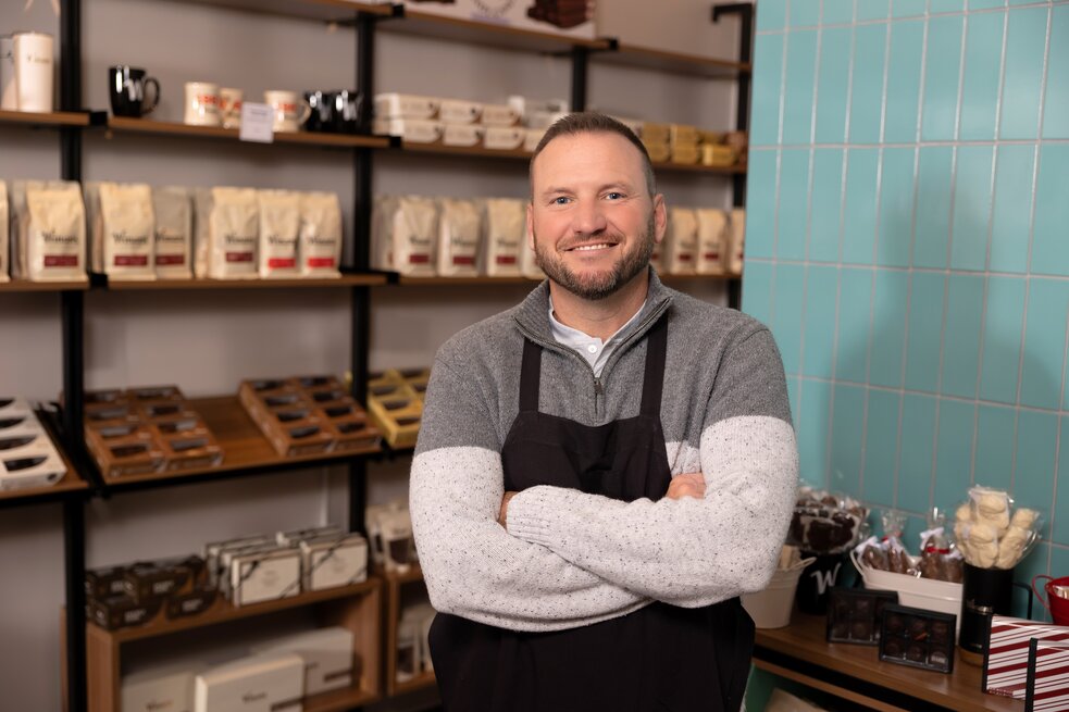Person in a striped apron using a red hand truck to move a large cardboard box inside a retail store