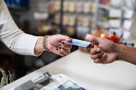 Barista pouring milk into a cup in a coffee shop, with coffee-making equipment and other patrons in the background.