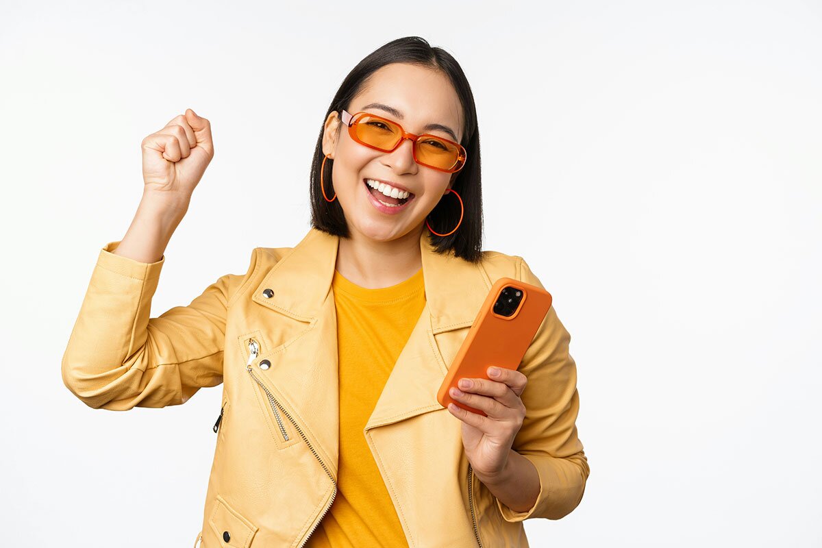 A happy woman dressed all in yellow, raising her hand with a phone in the other hand