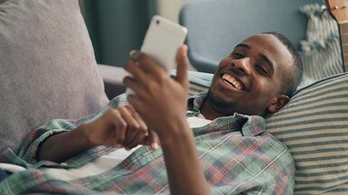 Happy man laying on a couch holding a cellphone in his hand.