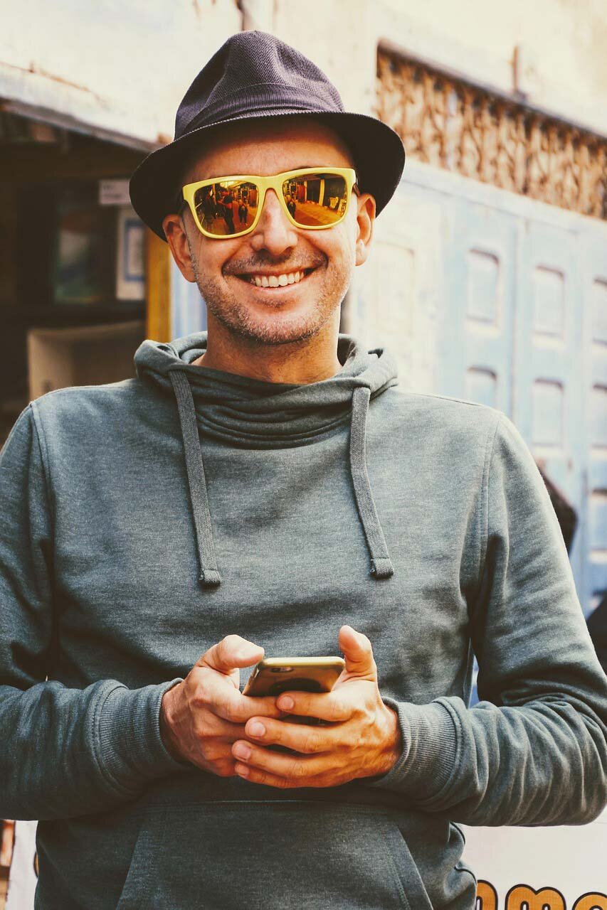 A happy man in a grey hood wearing sunglasses and holding a cell phone