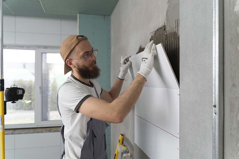 A handyman placing new tiles on a bathroom wall