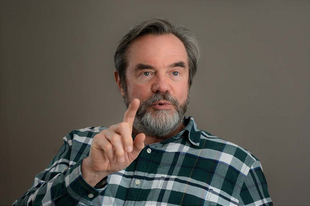 An older man talking with a finger lifted up