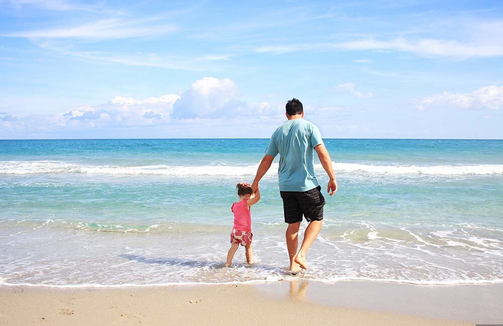 A father and daughter walking along the beach on their vacation.