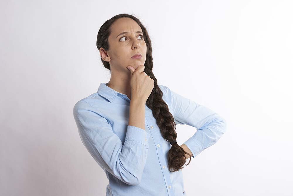 A woman standing in deep thought with an arm on her chin and waist