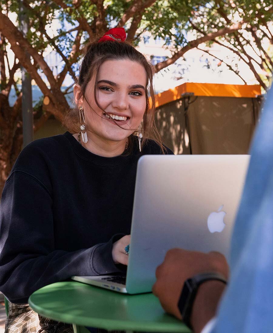 Smiling woman sitting at a table outside using a laptop