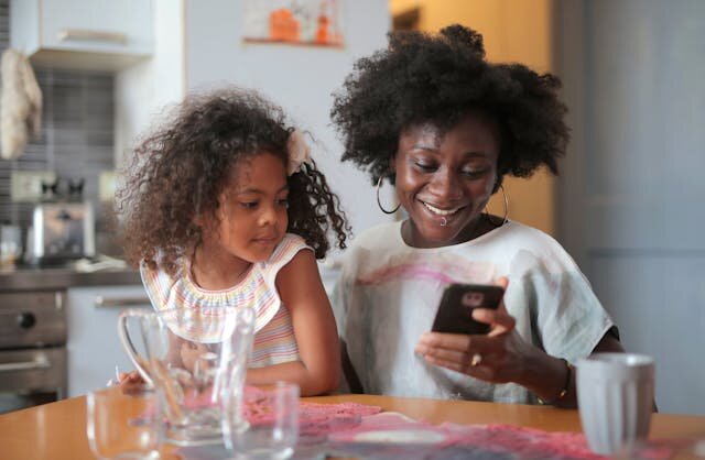 Smiling mother with young daughter reviewing Wisconsin loan approval on a smartphone.