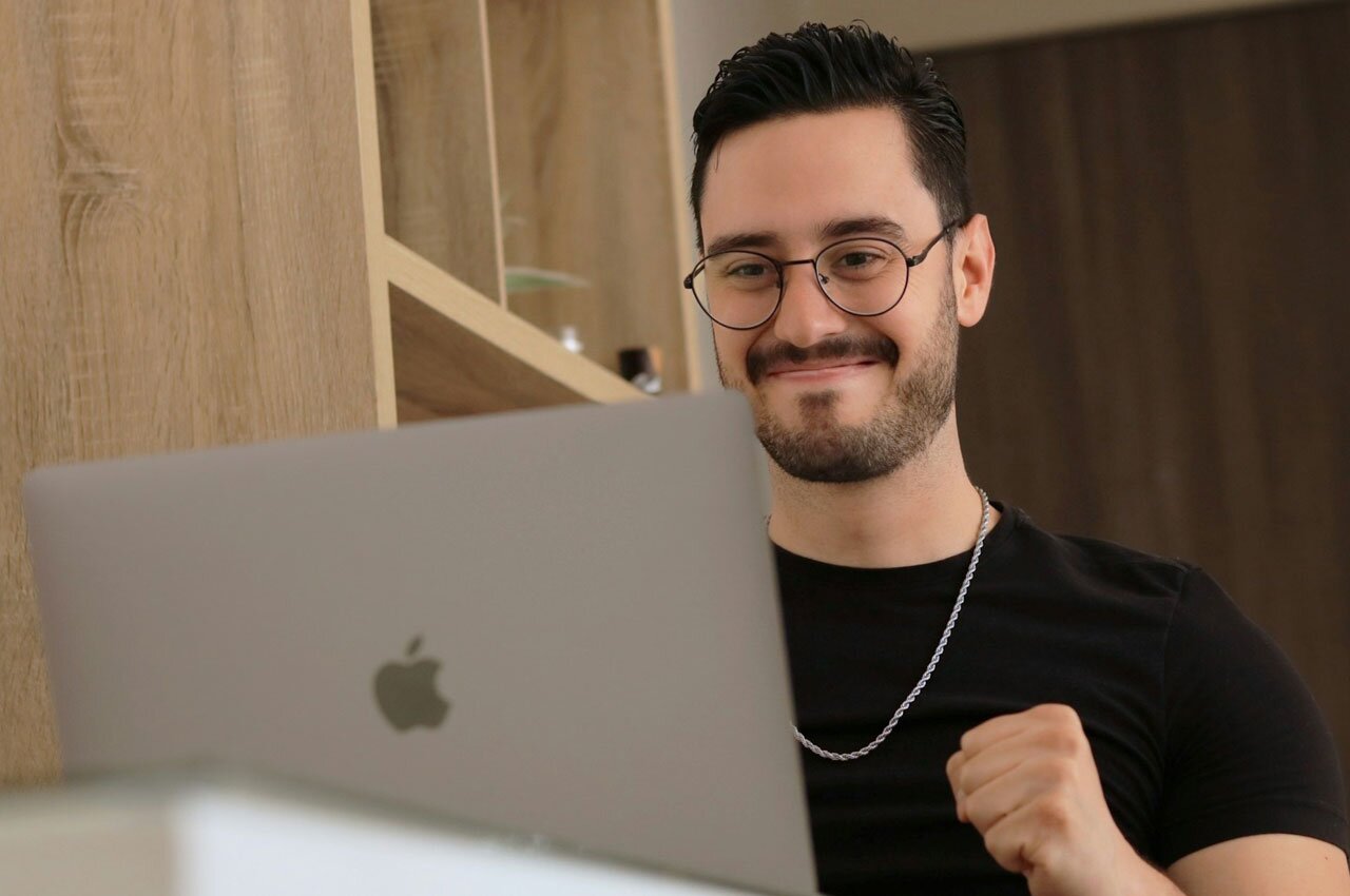 A man wearing glasses sitting at a desk looking at a laptop.