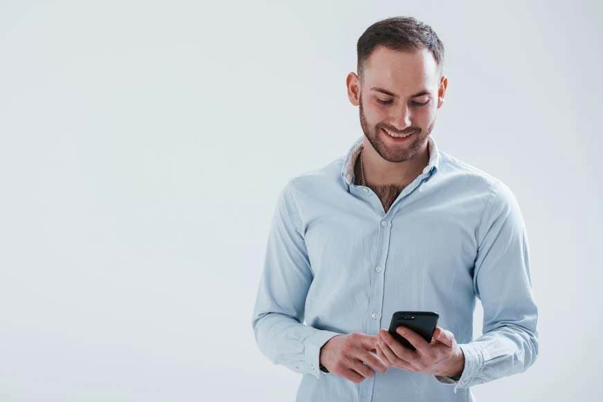 A man dressed in a button-down shirt smiles while using his phone to apply for a loan.