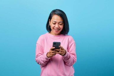 A happy woman in a pink shirt using a cellphone  to check her DTI ratio.