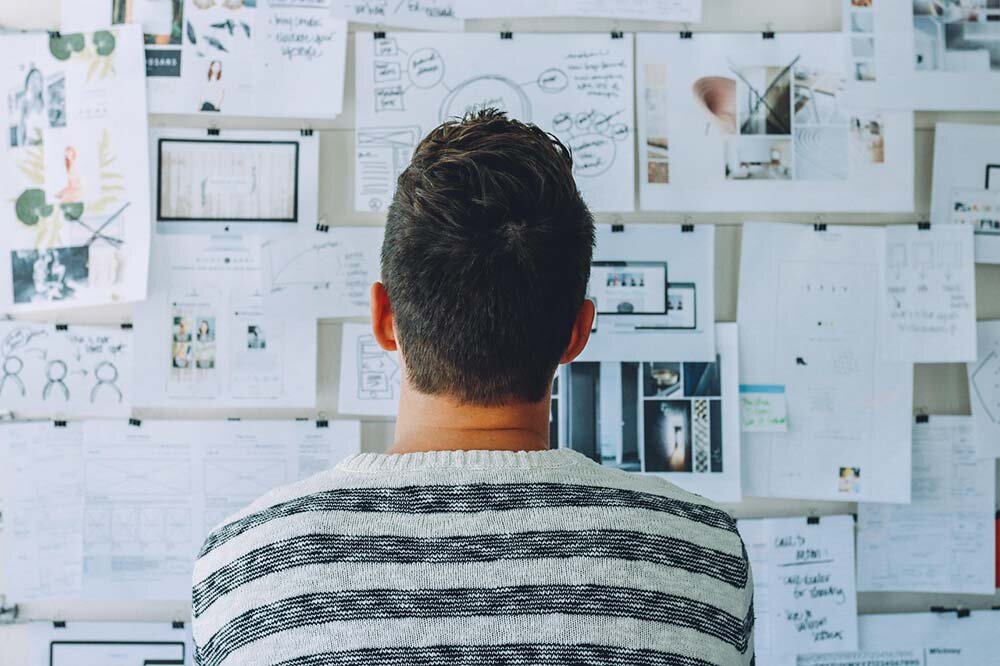 A man facing a whiteboard that has many papers fastened to it
