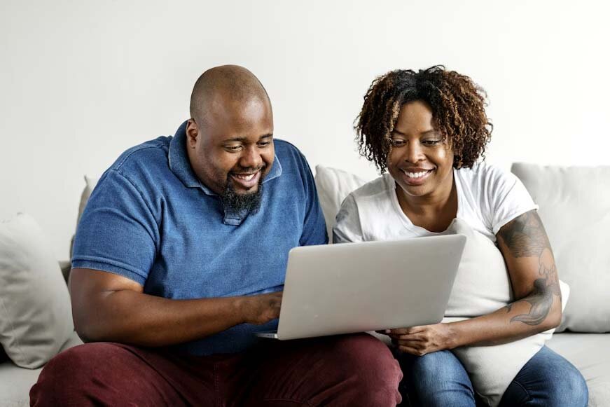 A couple sitting on a couch sharing a laptop.