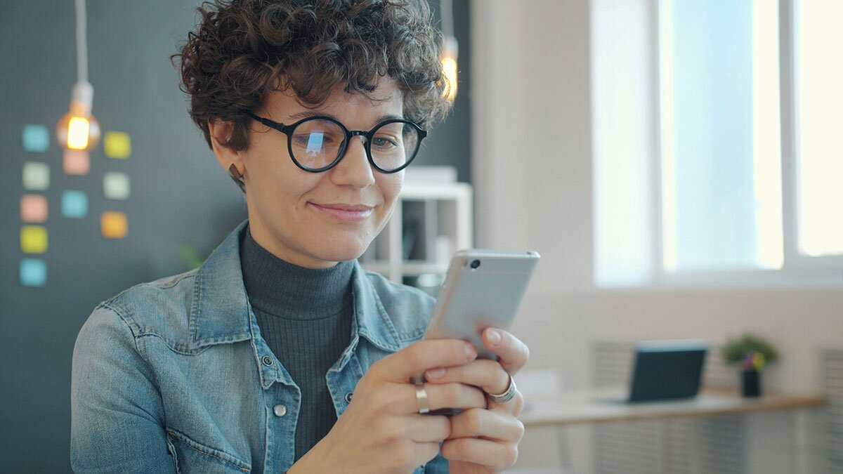 A woman smiling, holding her phone in both hands